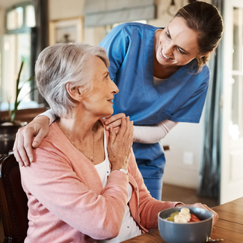 Krankenpflegerin kümmert sich um Seniorin am Tisch